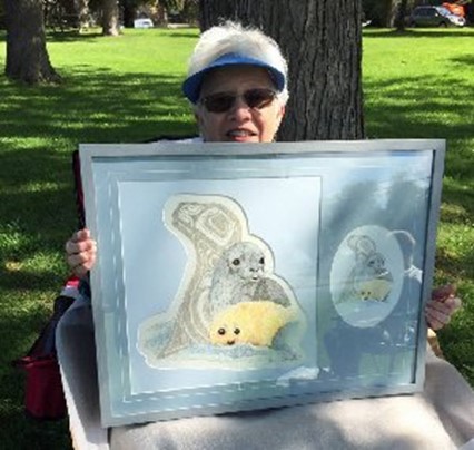 woman holds framed image of embroidered baby seals