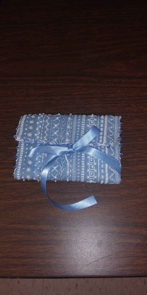 blue needlecase with rows of white embroidery