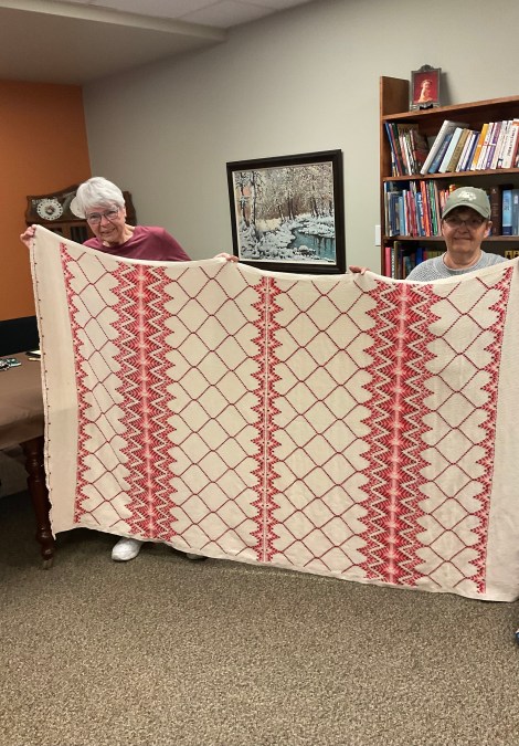 2 people holding bed-size blanket