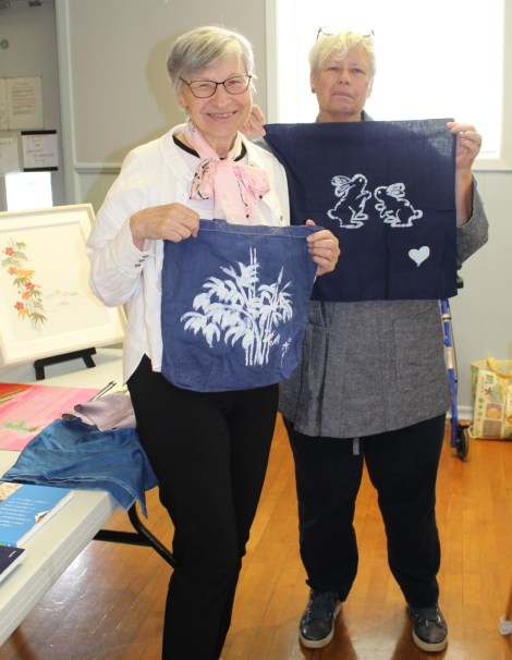 2 women, each holding white artwork on blue cloth
