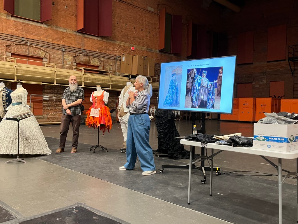 speaker on stage with costumes on mannequins