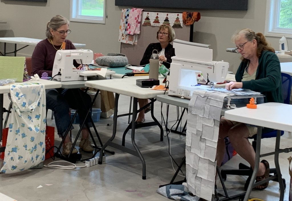 a group of 3 quilters at their sewing machines