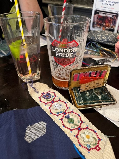 glasses of beer next to a cross-stitch piece and needlecase