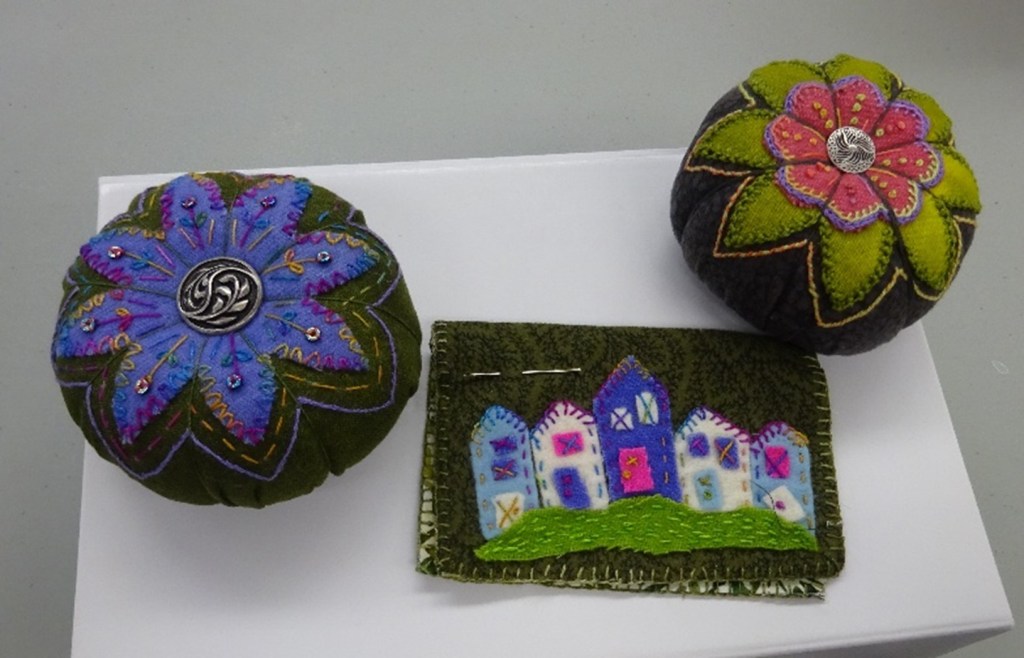 2 highly decorated pincushions and a small felt image of houses