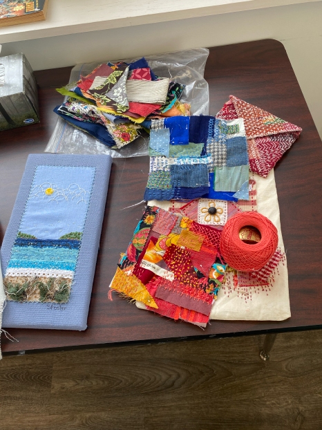 4 Boro samples on a table beside a spool of perle cotton, some fabric scraps and a small, embroidered landscape
