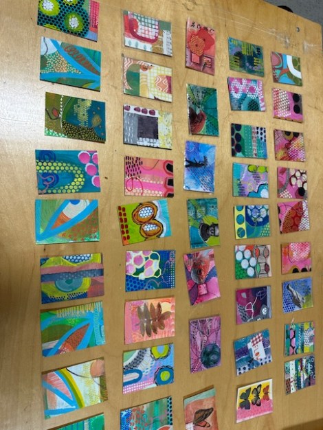 about 50 small, artist trading cards displayed on a wall