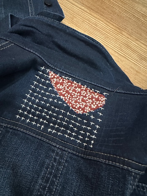 a piece of printed fabric stitched to the back of a jean jacket, in Boro style